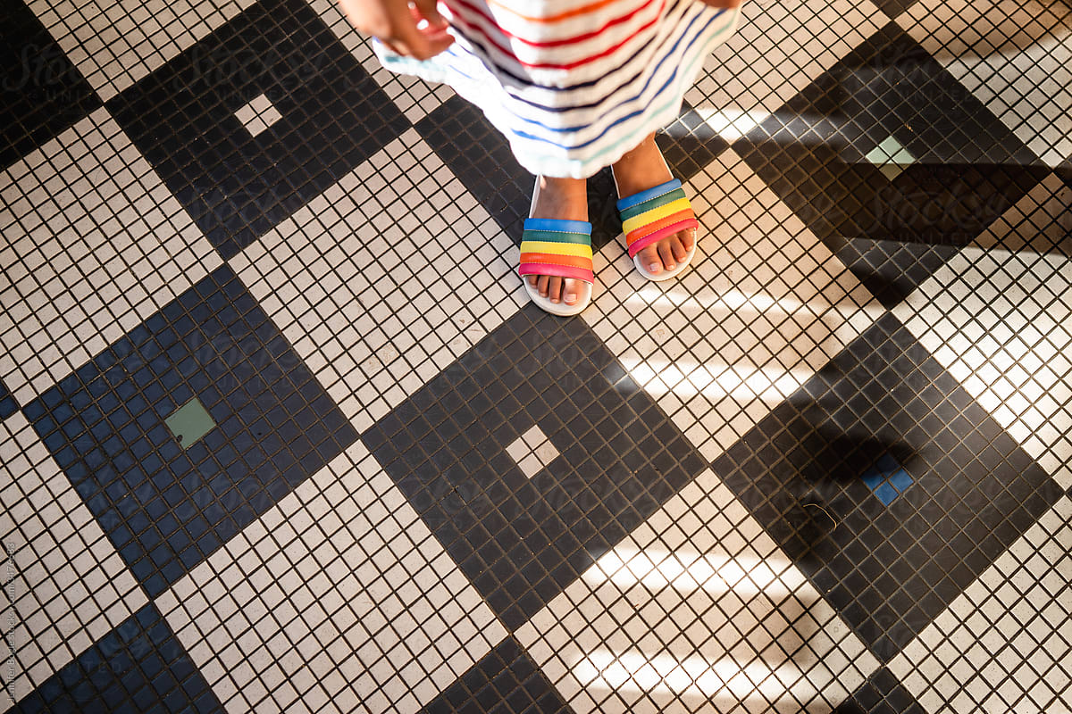 Feet of child in rainbow sandals on tile floor