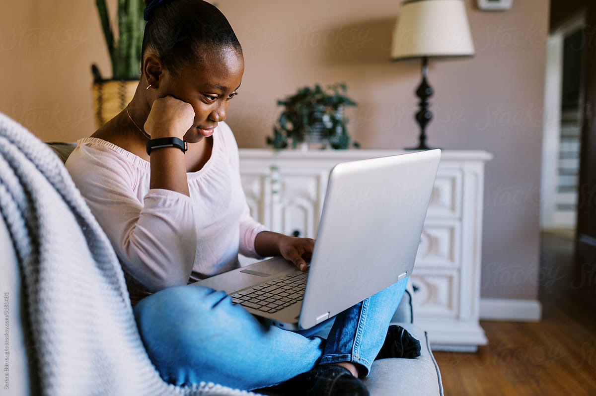 black girl sitting on couch in living room doing homework on laptop