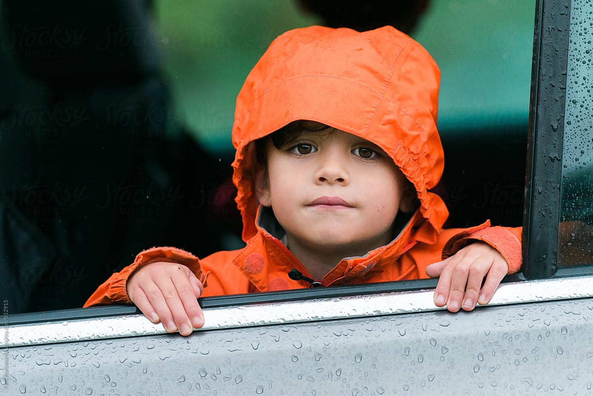 young child in orange raincoat looking out an open car window
