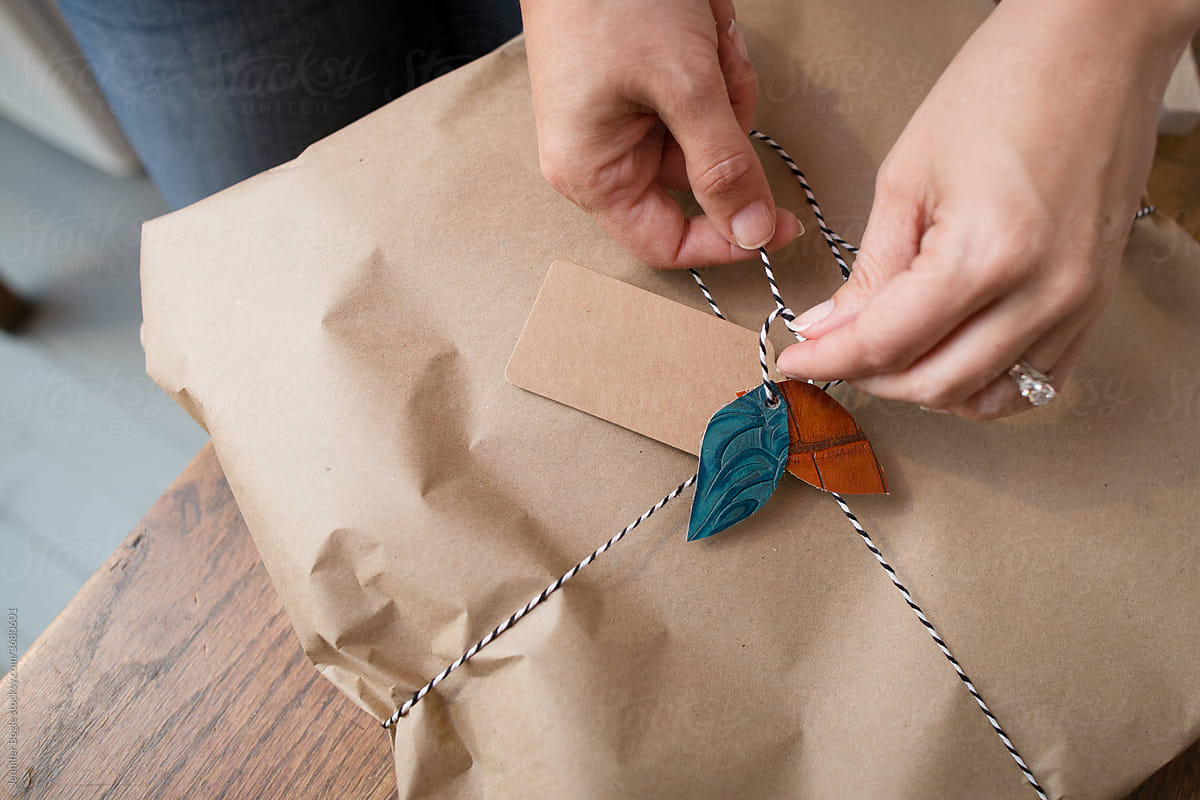 Hands tie leather leaves onto wrapped package