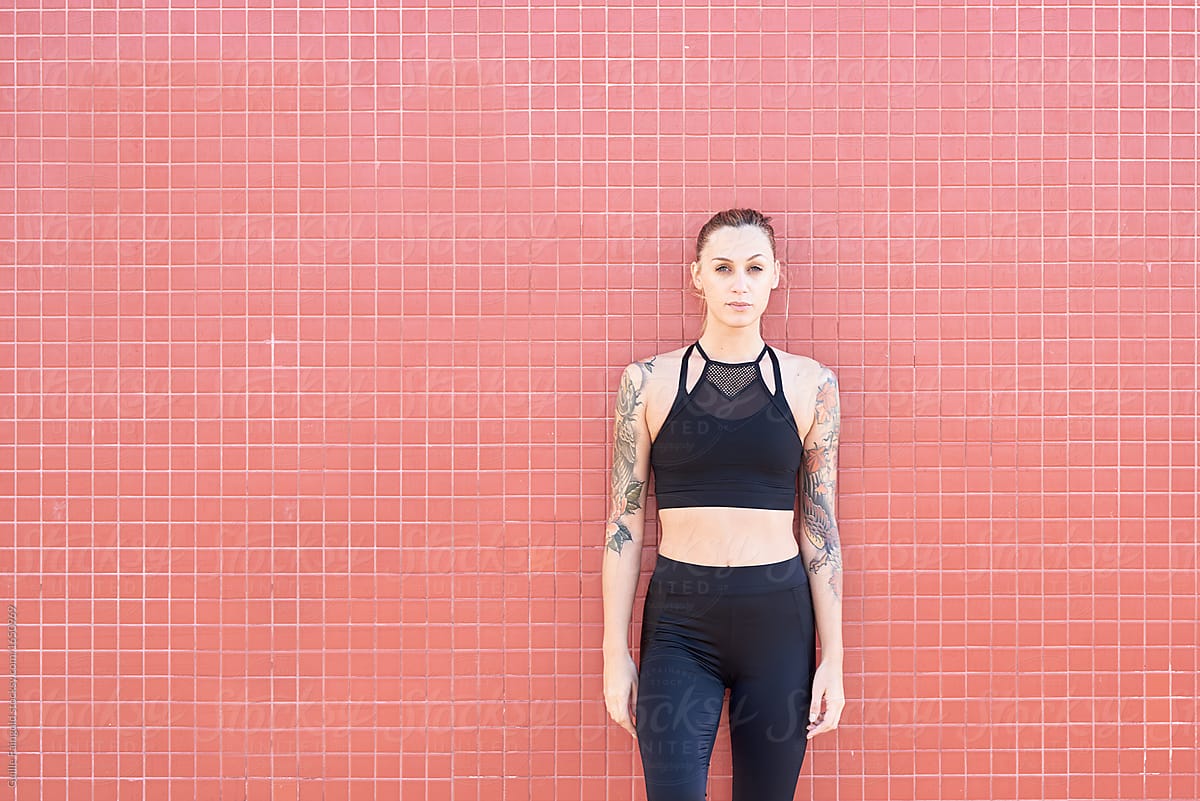 Sportswoman with tattooed arms over tiled wall.