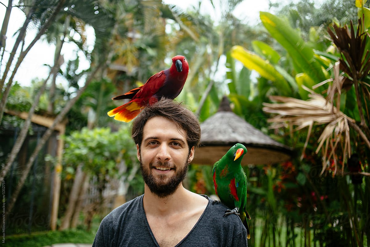 Young man with two birds on hi head looking at camera smiling