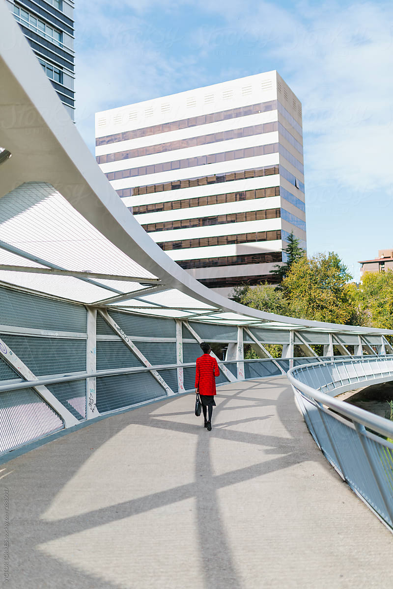 Elegant black woman in red jacket walking on geometric bridge construction in downtown