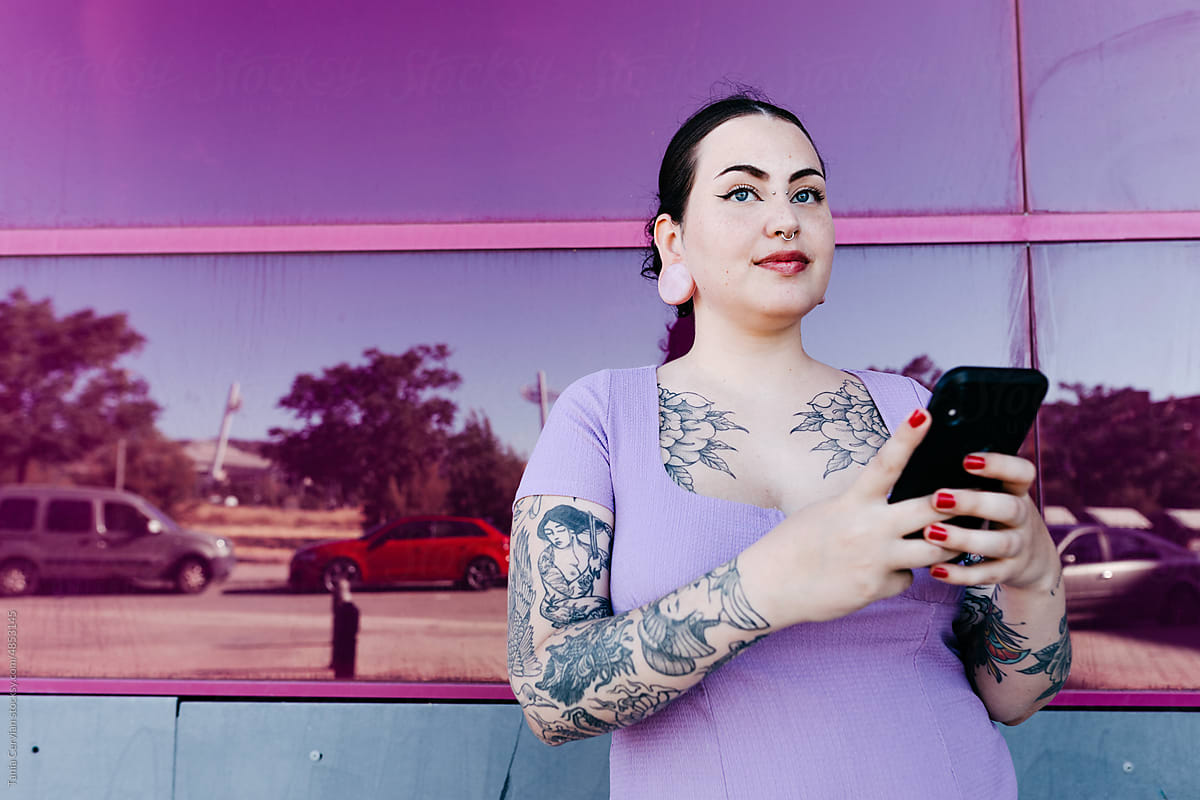 Tattooed curve model with smartphone against glass wall
