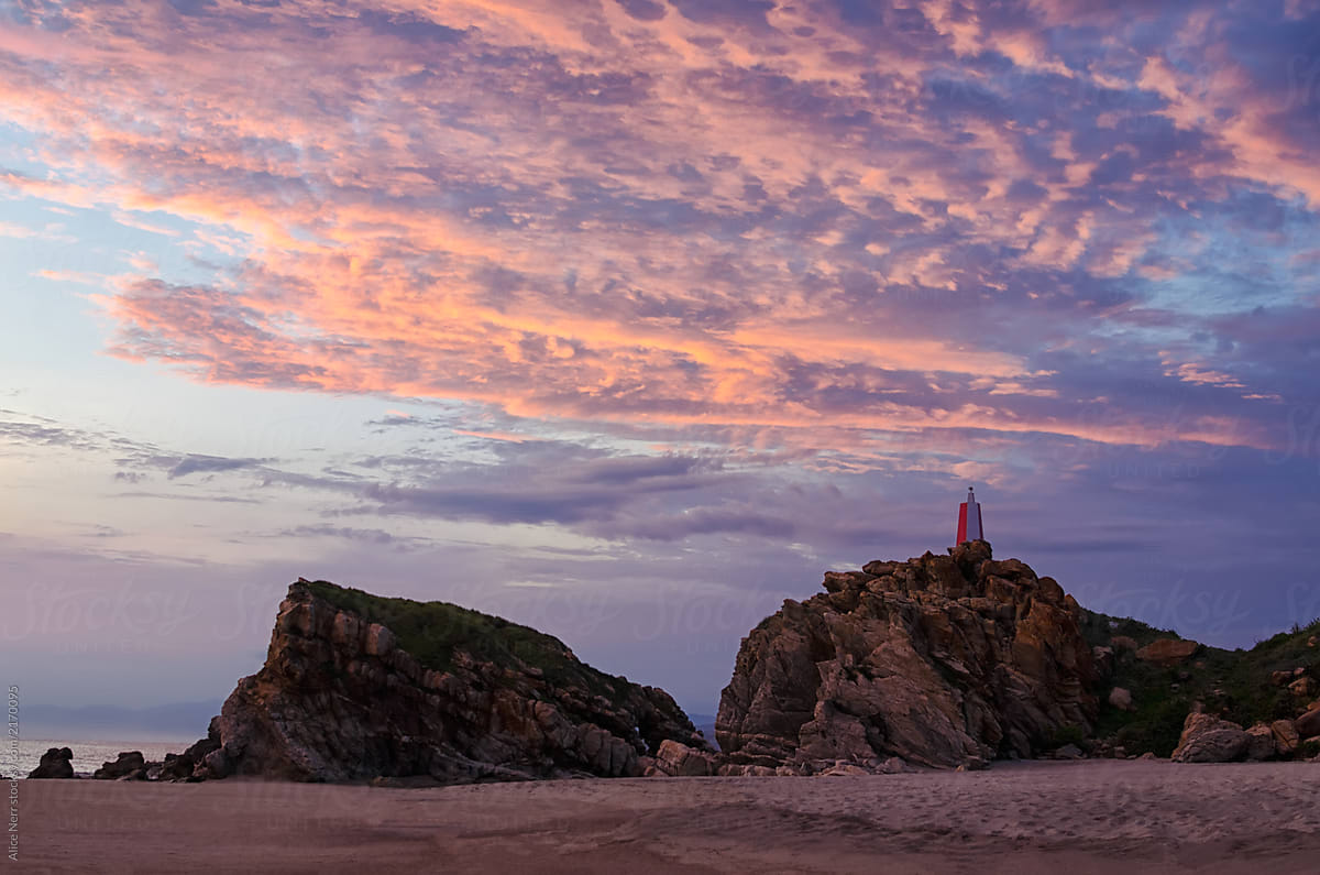 Stunning sunset at the beach over lighthouse on the rock