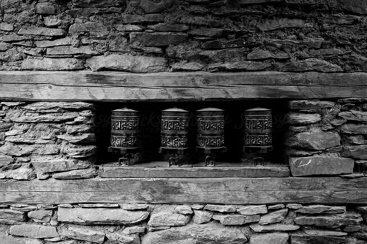 Black and white background of prayer wheels on a stone textured wall.