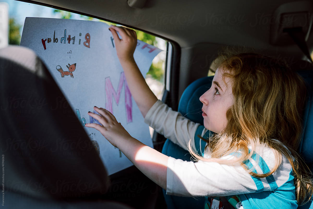 A little girl holds up a sign in her car window.