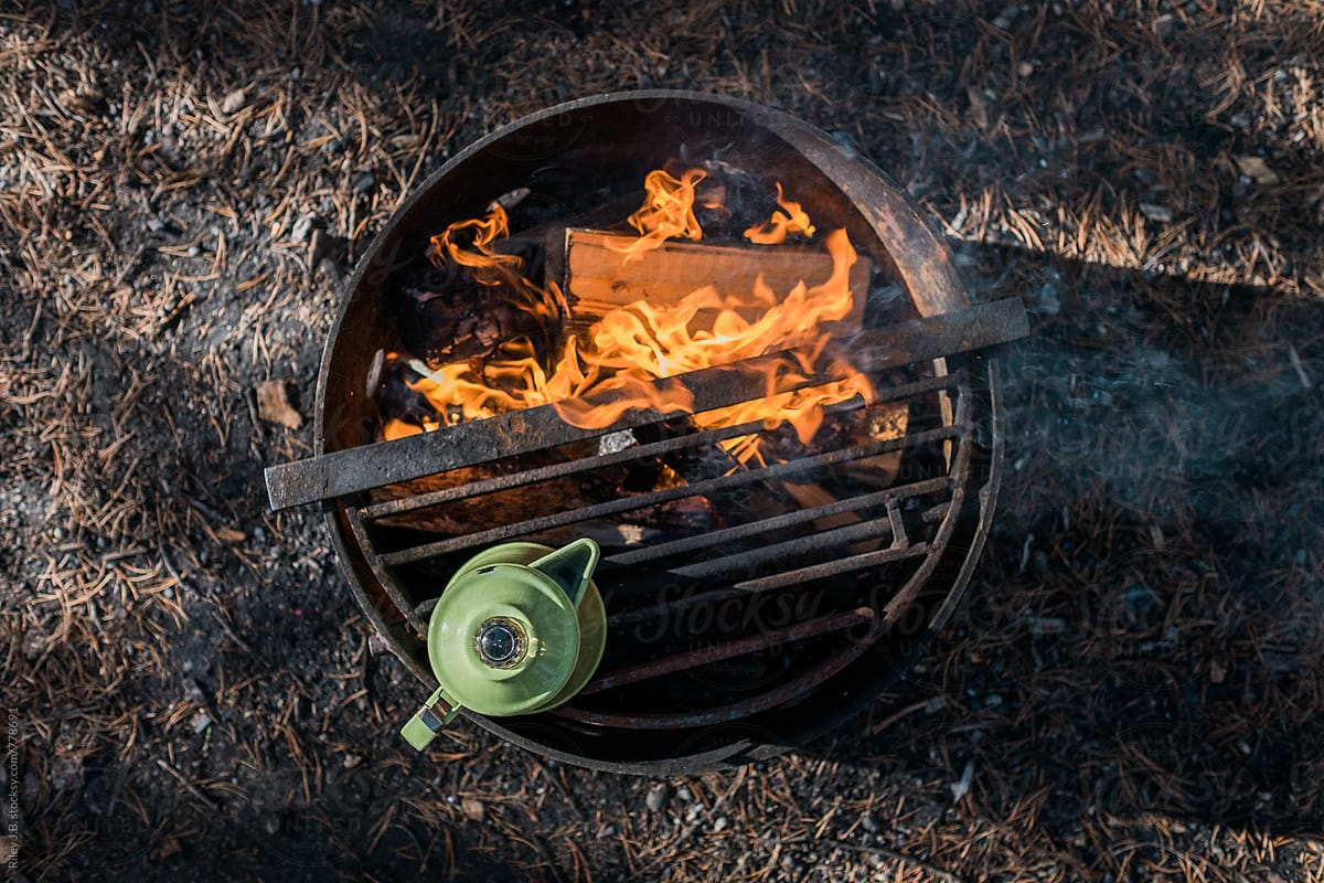 A enameled kettle sits atop a camp fire viewed from above