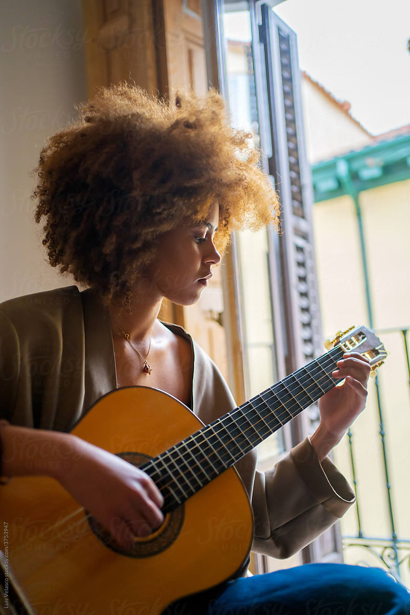 Black Woman Playing Music With The Guitar Next To The Window.