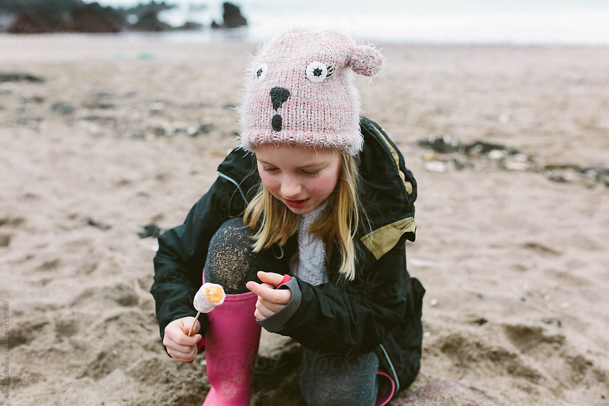 Little girl toasting marshmallows over a fire on a beach in winter