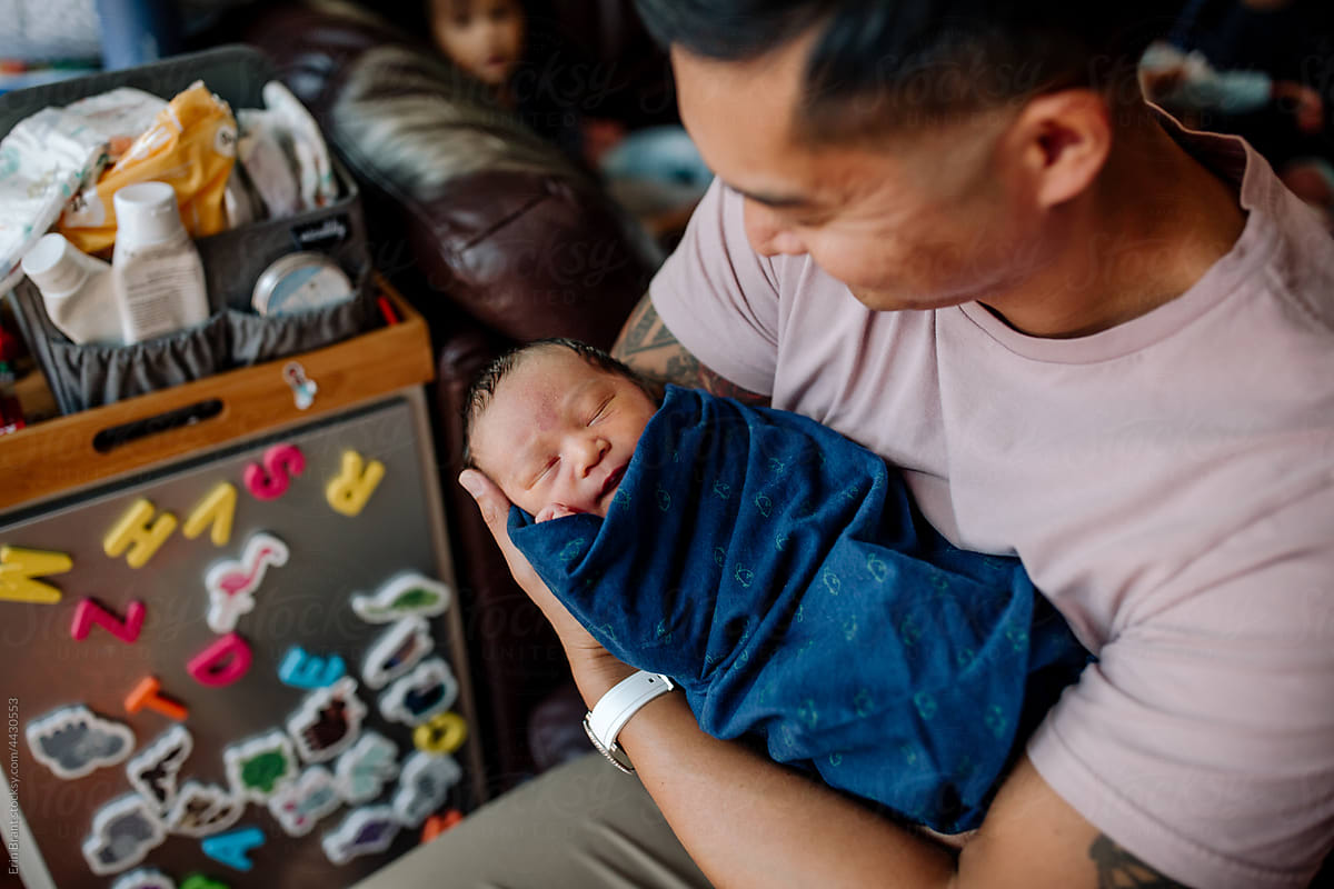 Smiling new dad holding newborn son in his home