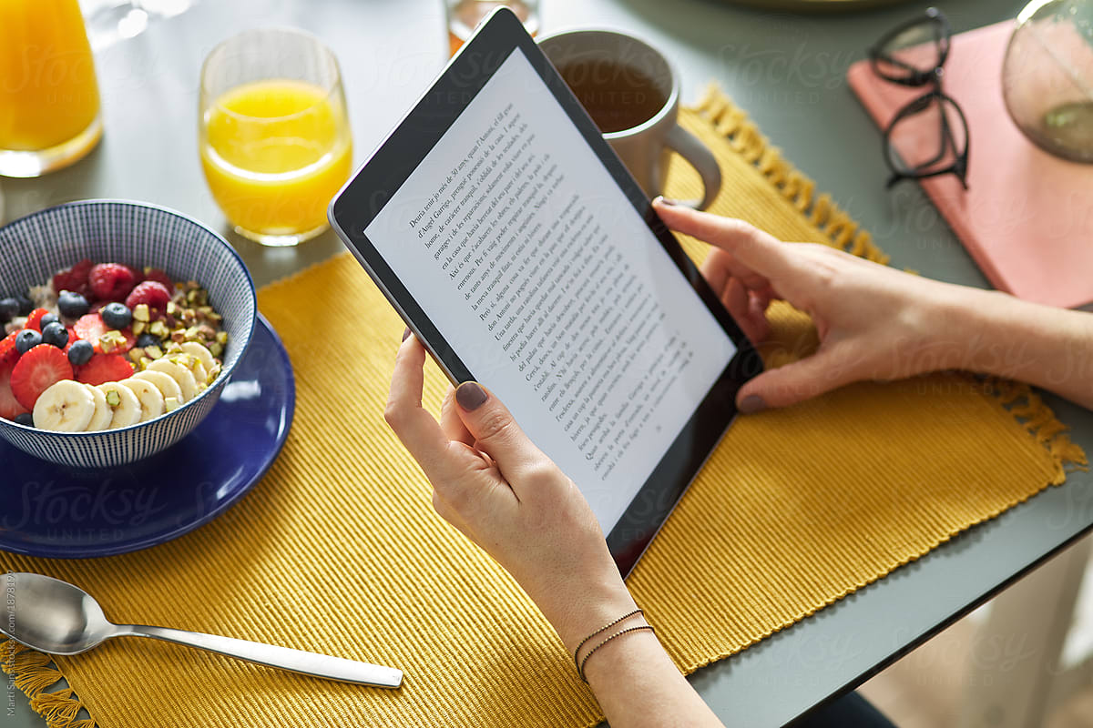 Woman reading via tablet while having breakfast at home