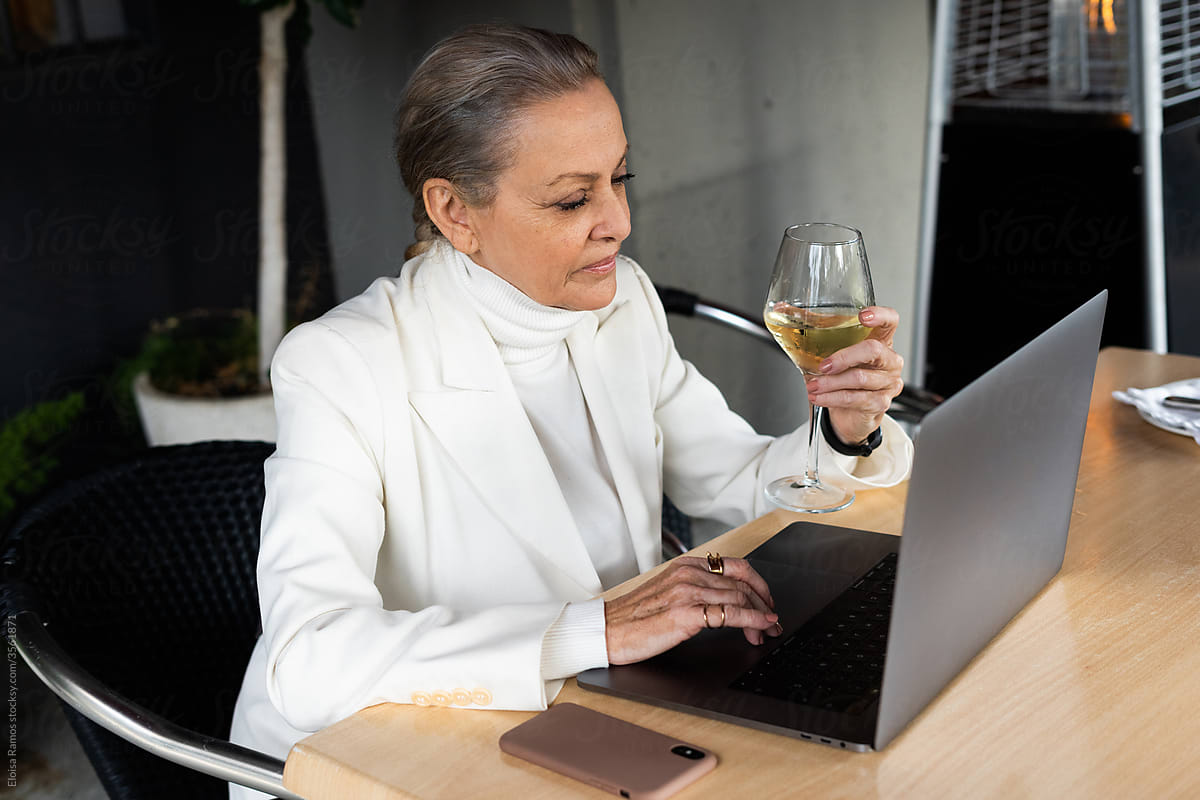 senior business woman checking  laptop and drinking a cup of wine at restaurant