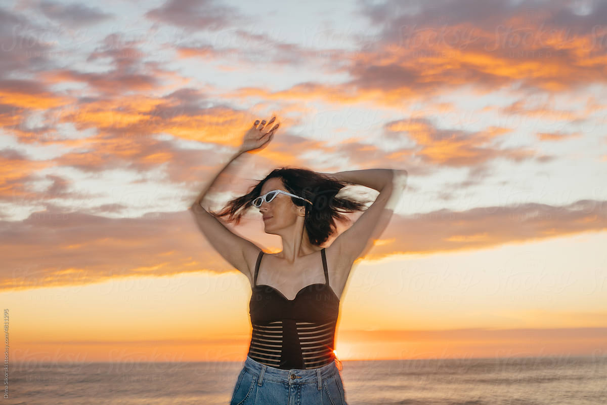Dancing girl in fashionable sunglasses on the beach at sunset