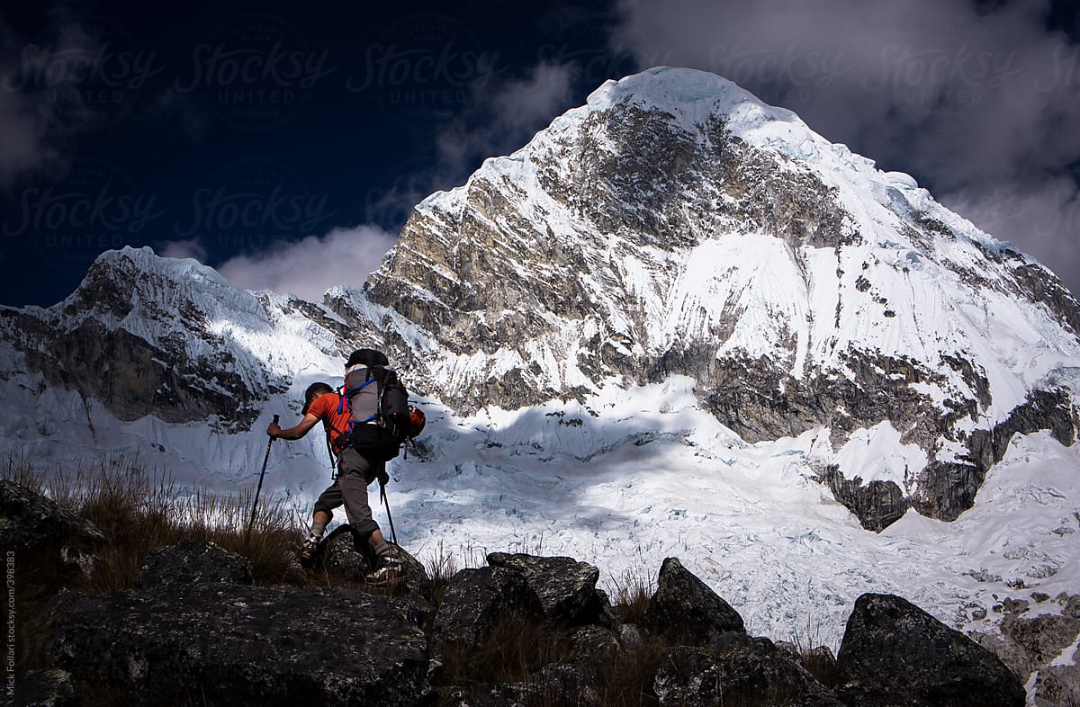Mountain climber with large pack crosses in front of dramatic high altitude mountain