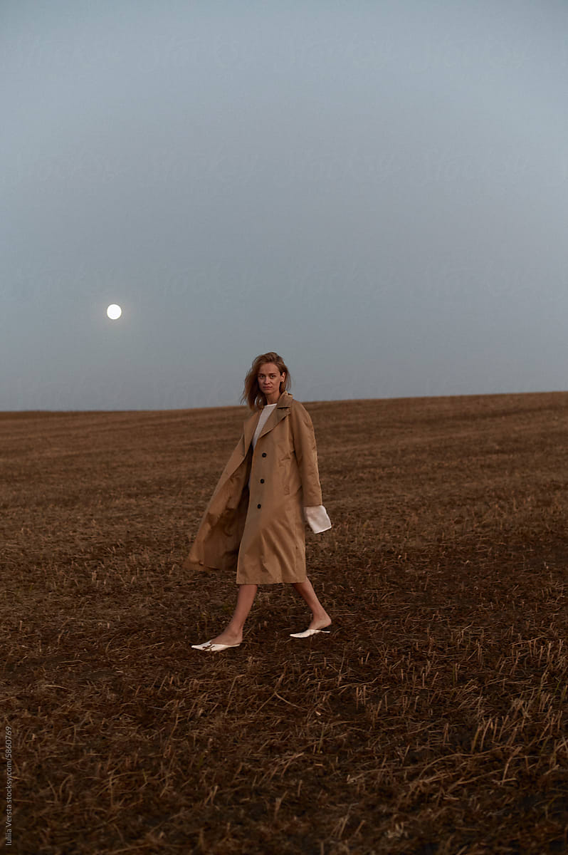 a woman in a raincoat walks in the field under the moon