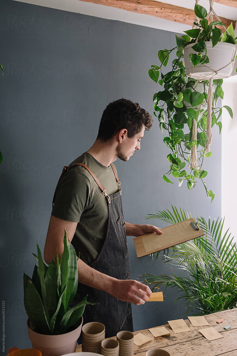 Man Brainstorming With Notes Surrounded By Plants On Shelf