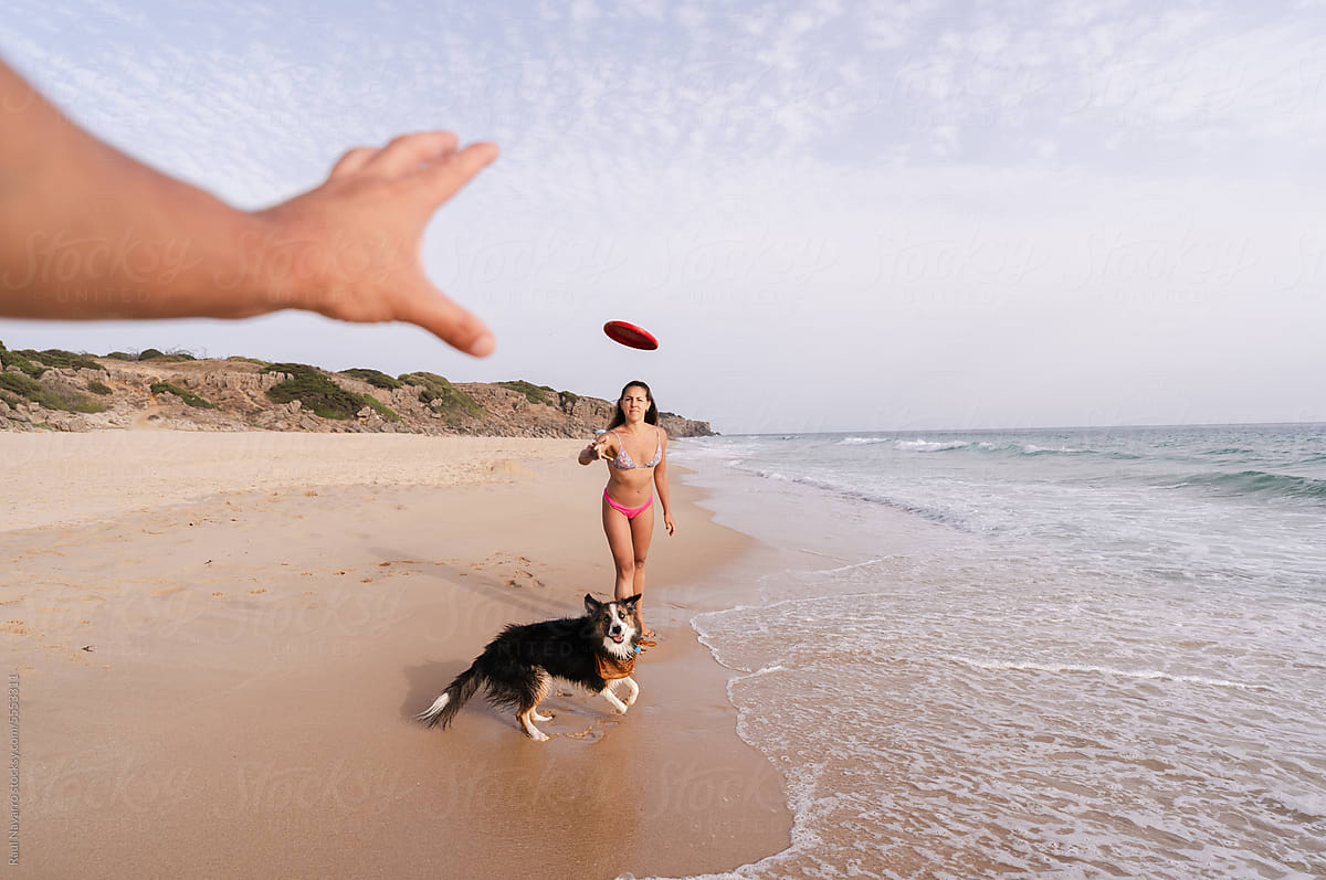 woman throwing a frisbee at a person on the beach with her dog.