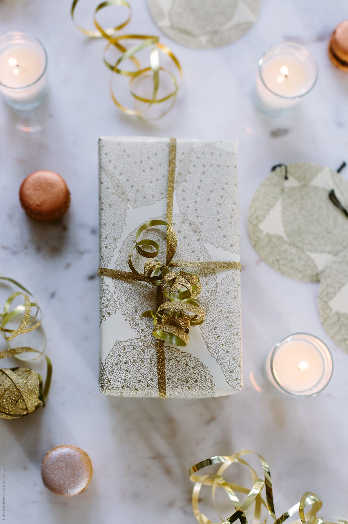 Gold theme wrapped Christmas gift with ribbon, candles and macaroons.