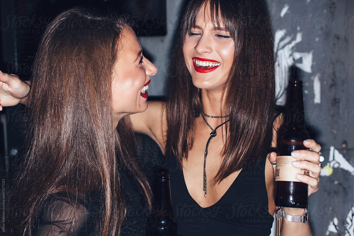 Two smiling nightlife girlfriends outdoor with beer