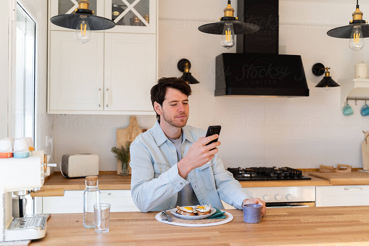 Portrait of happy man having breakfast and using phone
