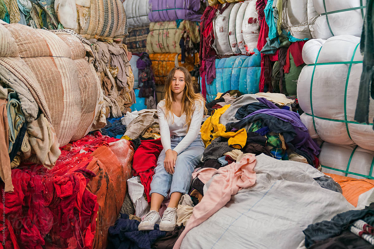 Young Woman Sitting on Piles of Used Clothes