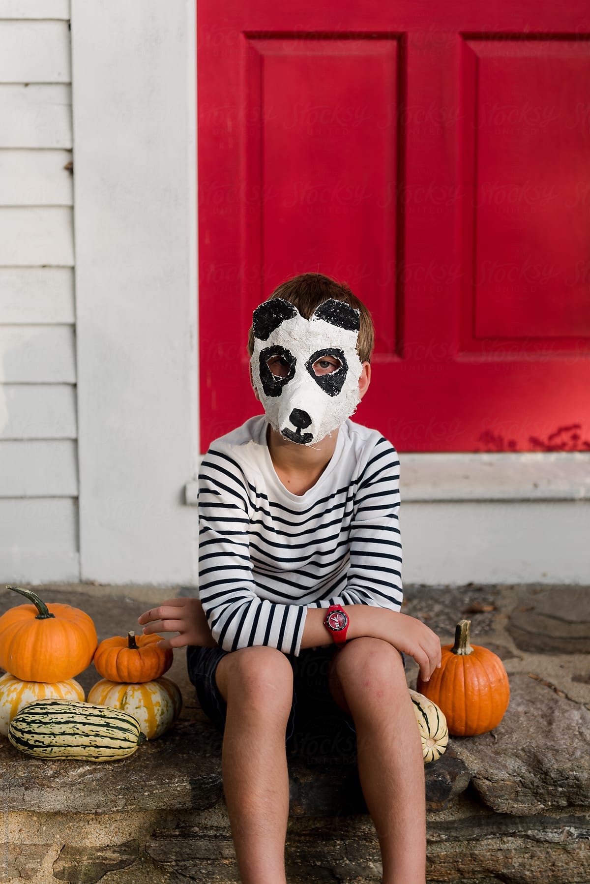 little boy in front of red door with panda bear mask in the fall