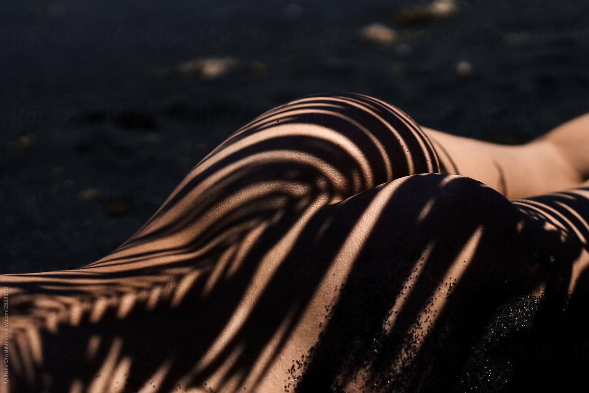 nude ass with palm shadows lying on the black sand