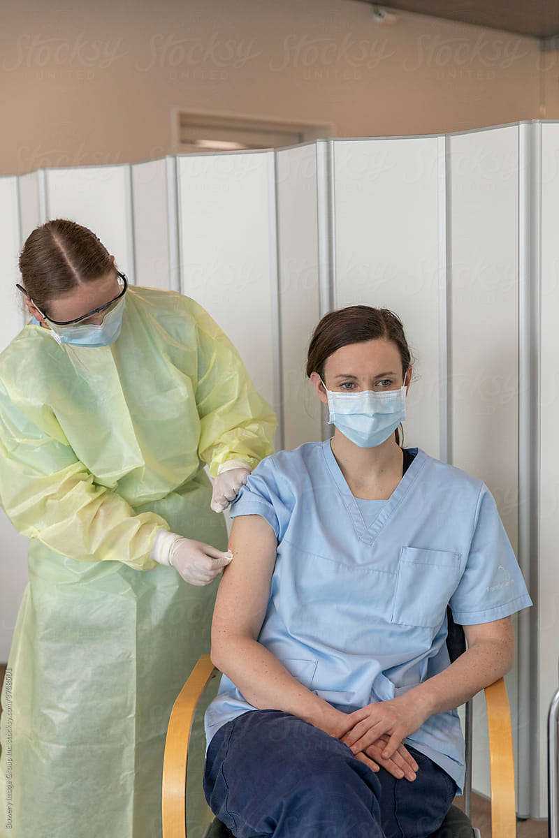 Person in a surgical mask receiving a needle in her right arm