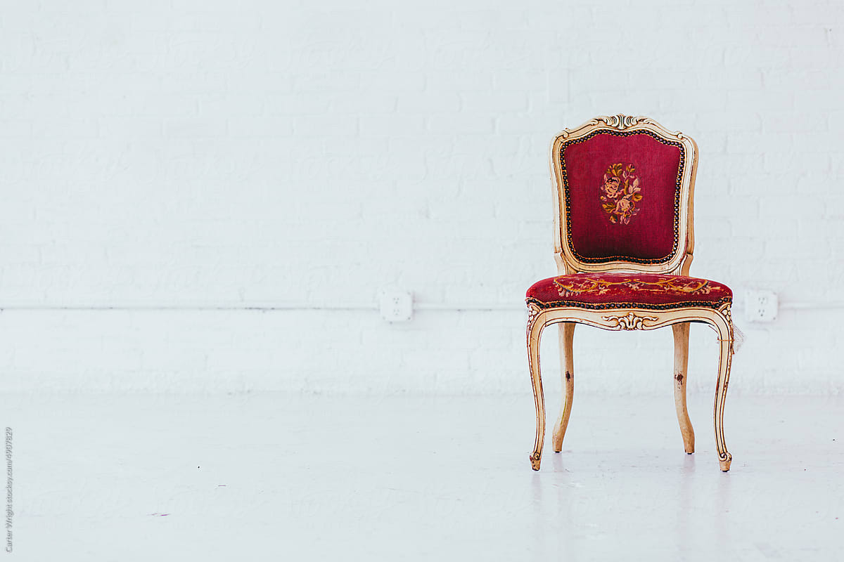 Vintage red embroidered chair seat with golden legs in a white studio
