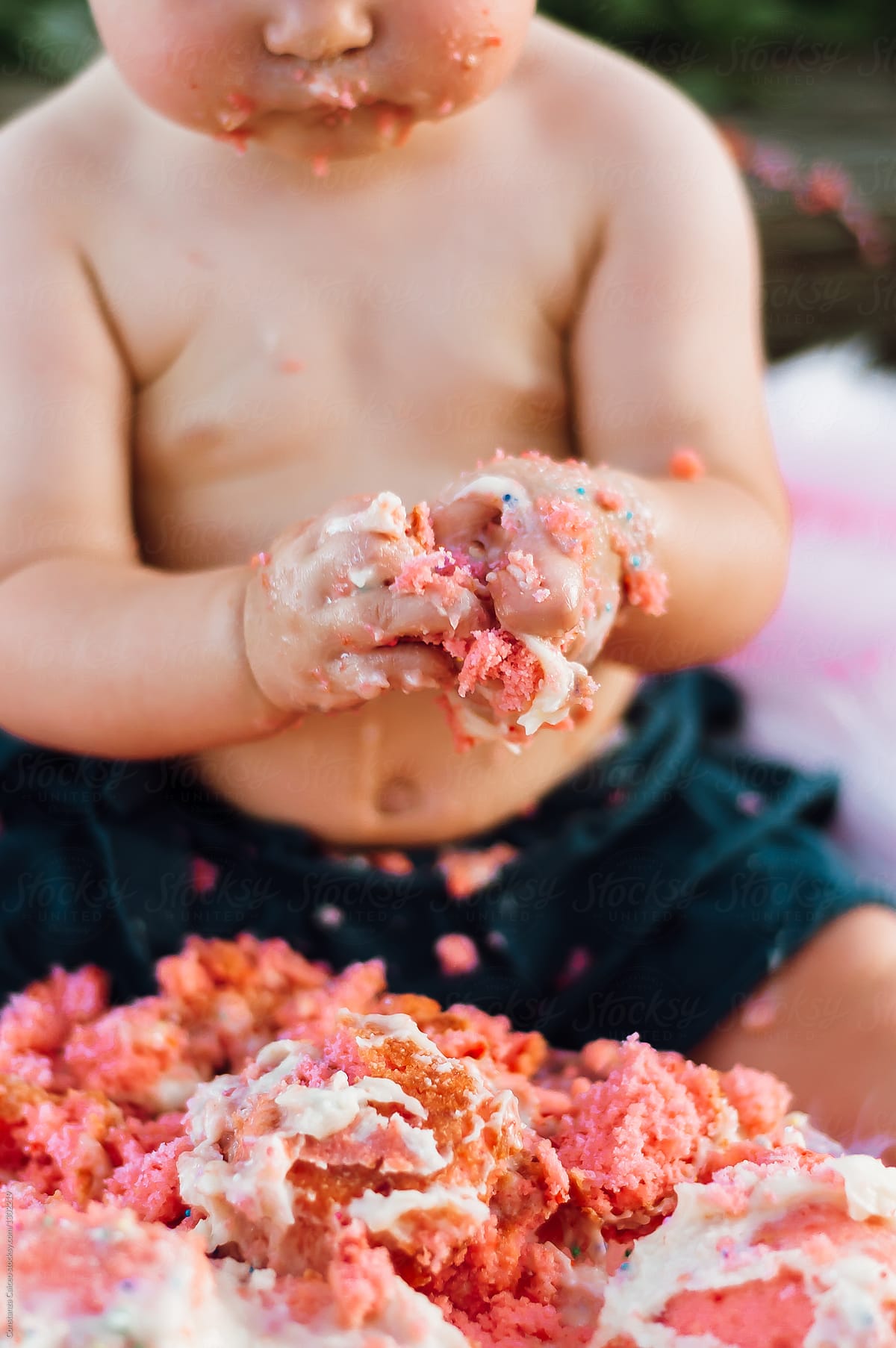 Baby\'s hand smashing a bright pink sugary cake