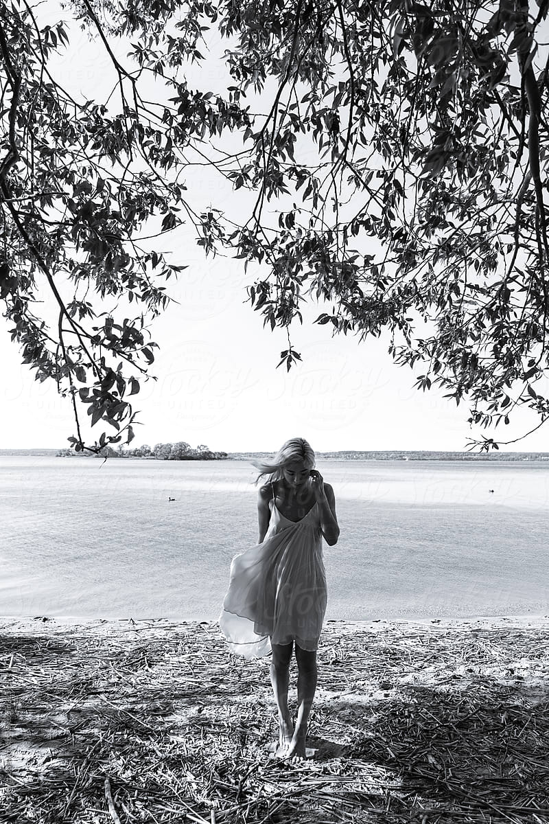 black and white photo of a girl in a light dress flying in the wind against the background of a lake and trees in nature
