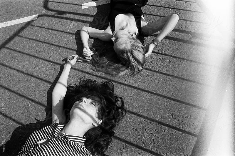 A black and white film portrait of two beautiful young woman lying on the ground