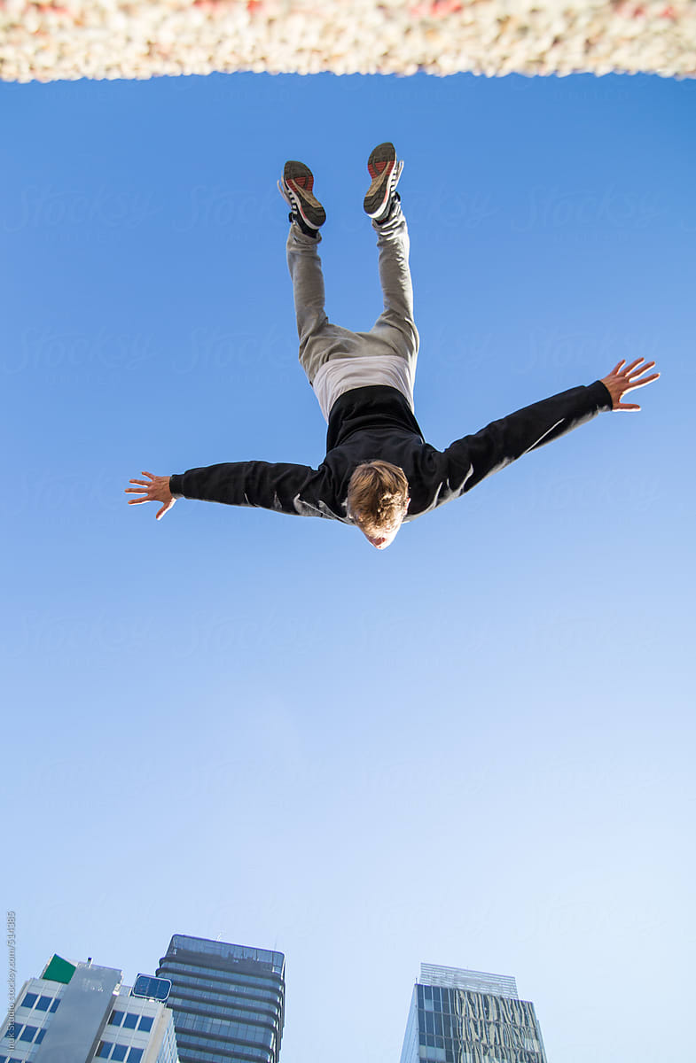 Nadir photography of a man doing a backflip in the air during a parkour training in a city