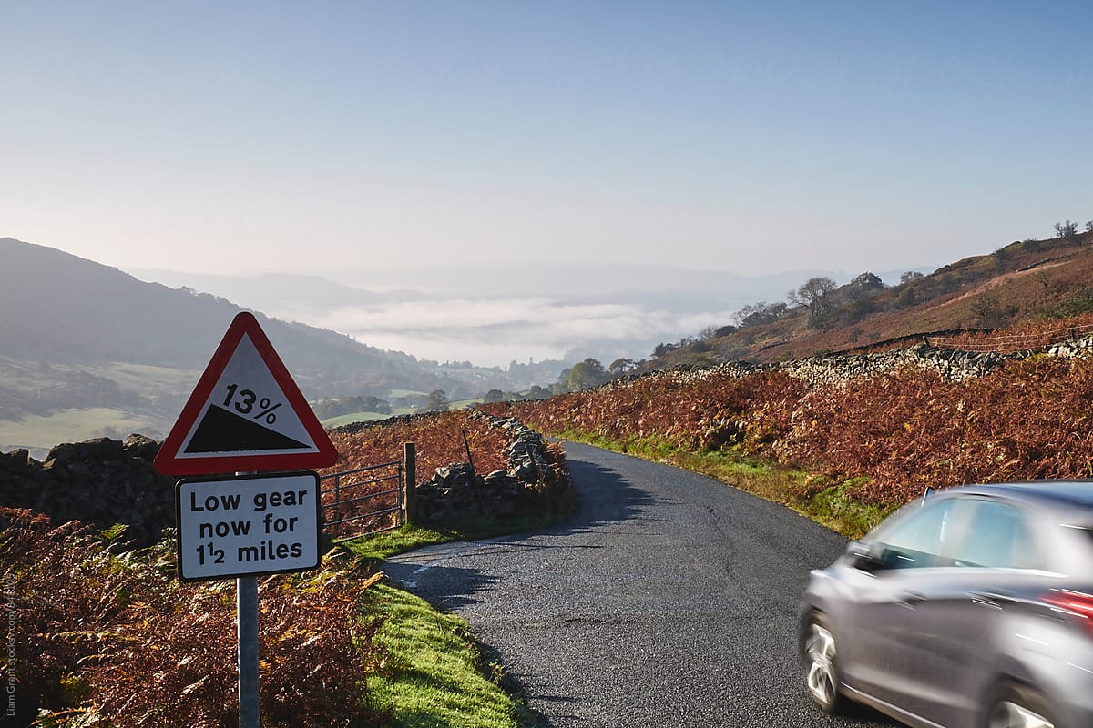 Steep road warning sign and fog in the valley. Cumbria, UK.