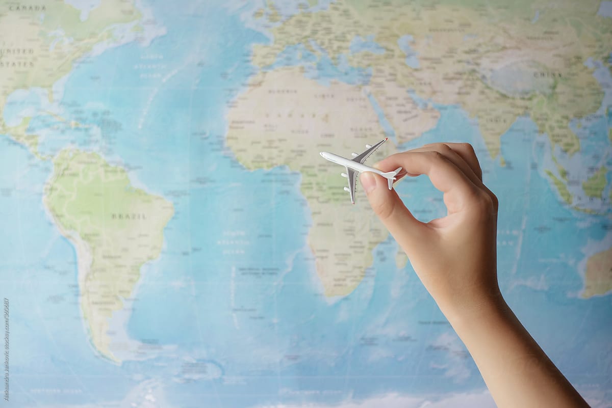 Person holding a small airplane in front of the world map