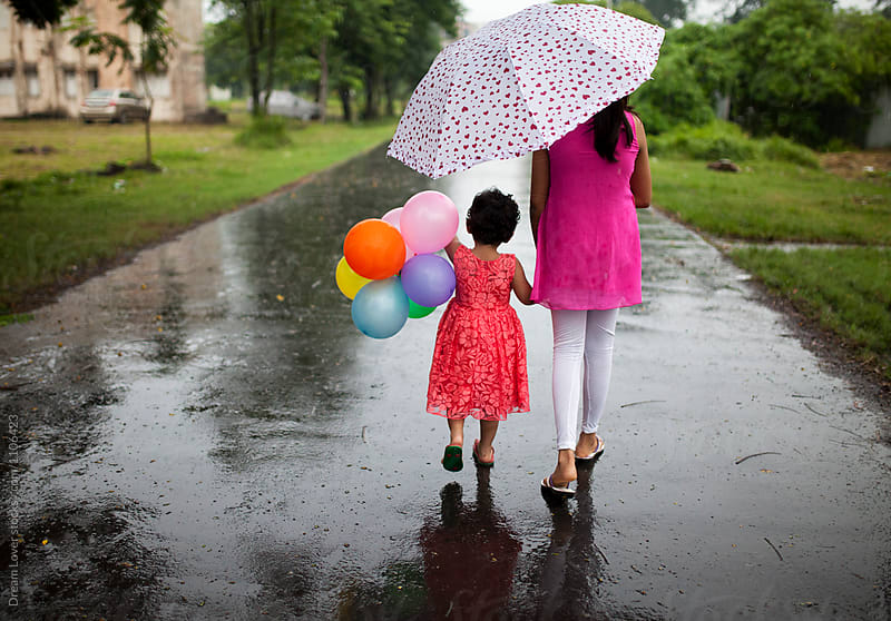 Little girl with elder sister walking together with umbrella with balloon in hand of the kid