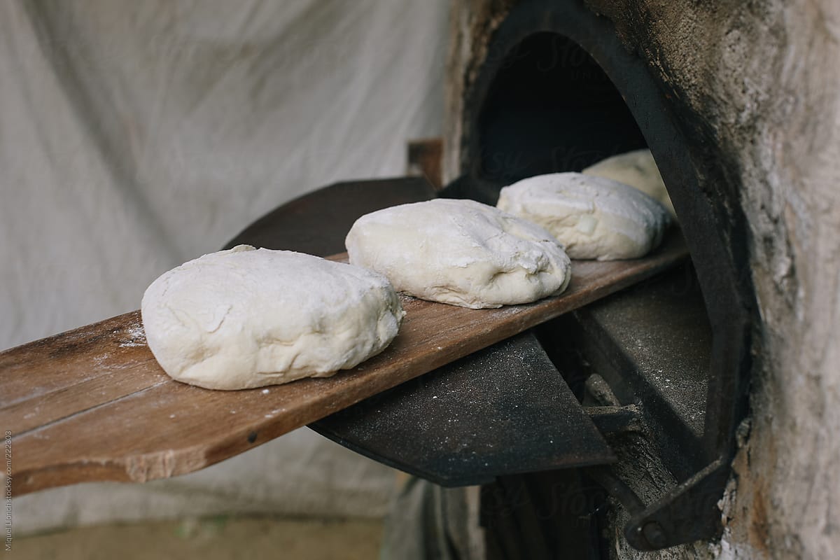Old traditional wood oven with bread loafs going inside.