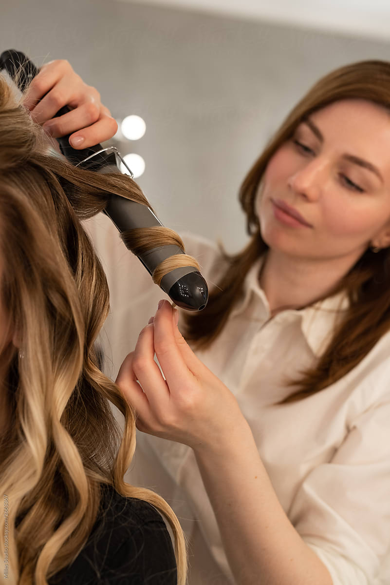 Female hairdresser styling hair with curling iron