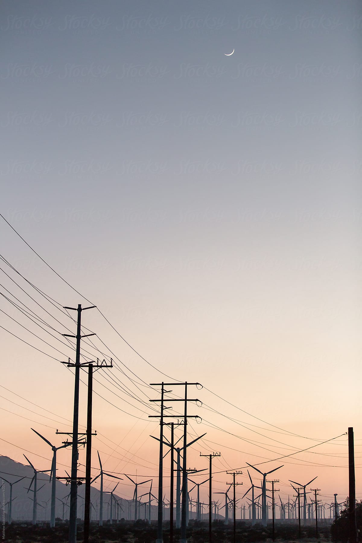 Power cables and wind turbines on landscape at sunset