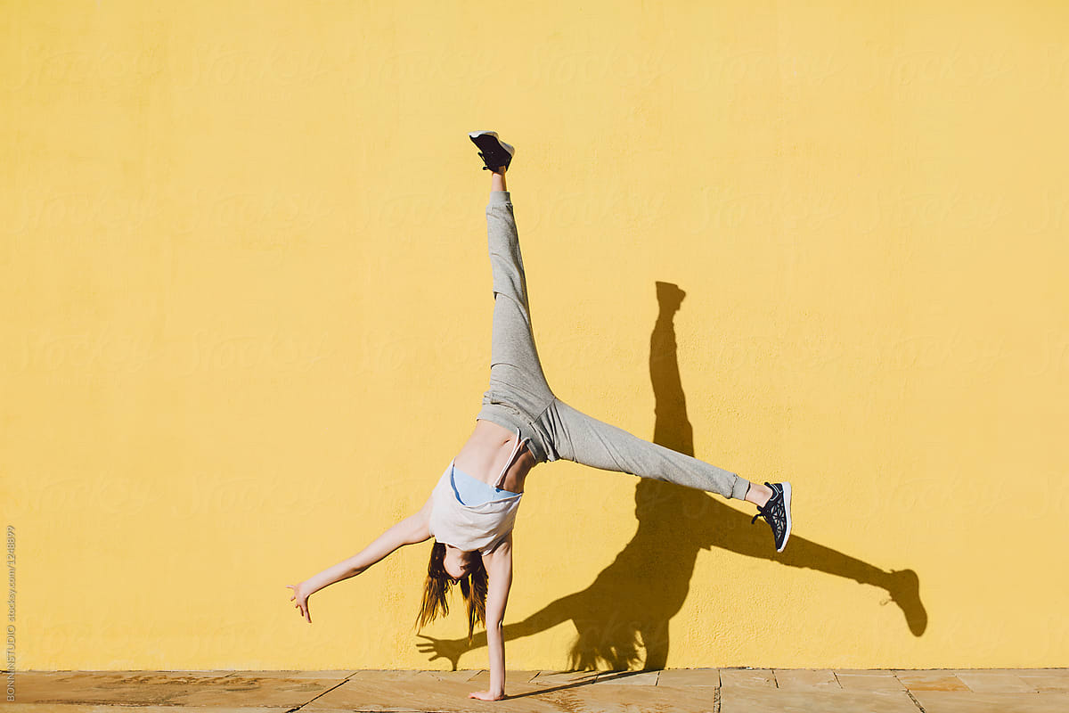 Young Woman Doing Handstand In Front Of A Yellow Wall. by Stocksy