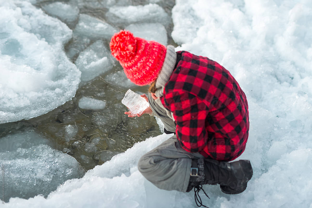 Girl examines ice kneeling by shore of Ontario lake