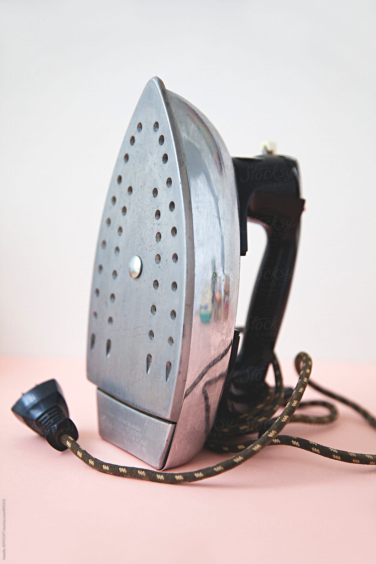 A retro household iron against a pink and white background