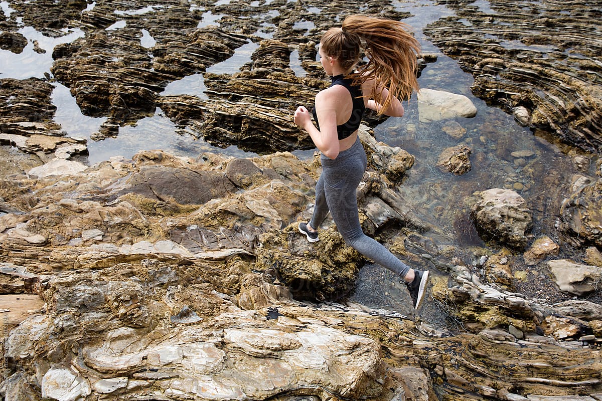 Athletic female running on rocks at the beach