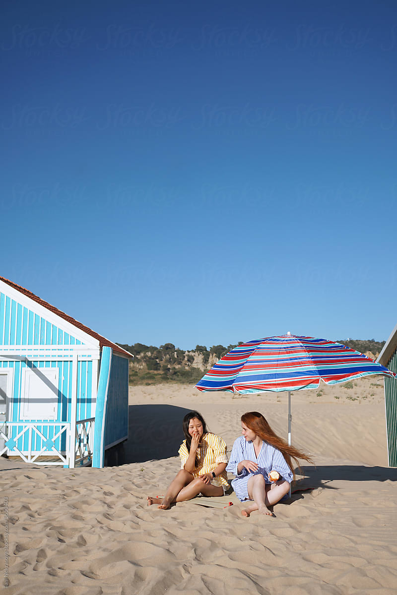 Young women sitting together on the sand by the ocean