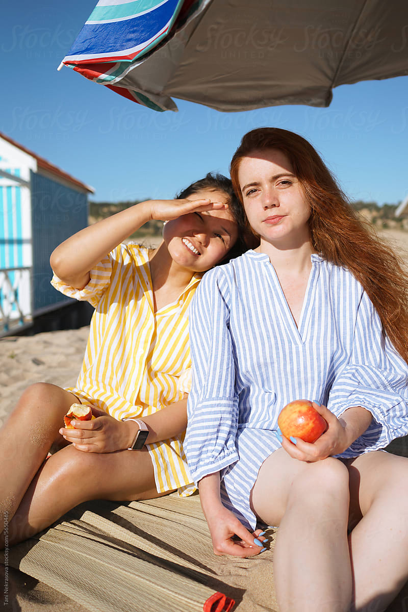 Two girls sitting on the beach and eating apples
