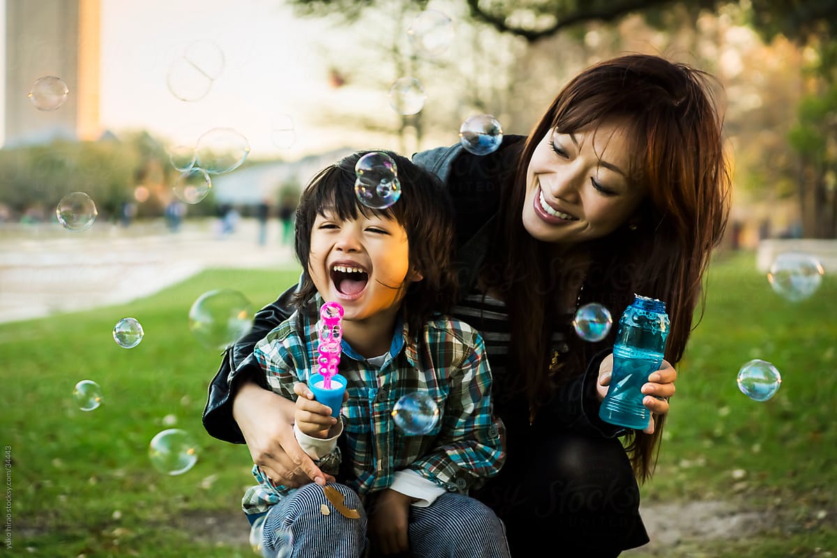 Asian Mother And Son Blowing Soap Bubbles Outdoors By Stocksy