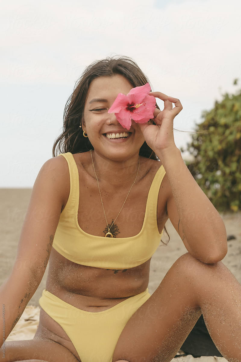 Asian girl in bikini is sitting at the beach with a flower in her face