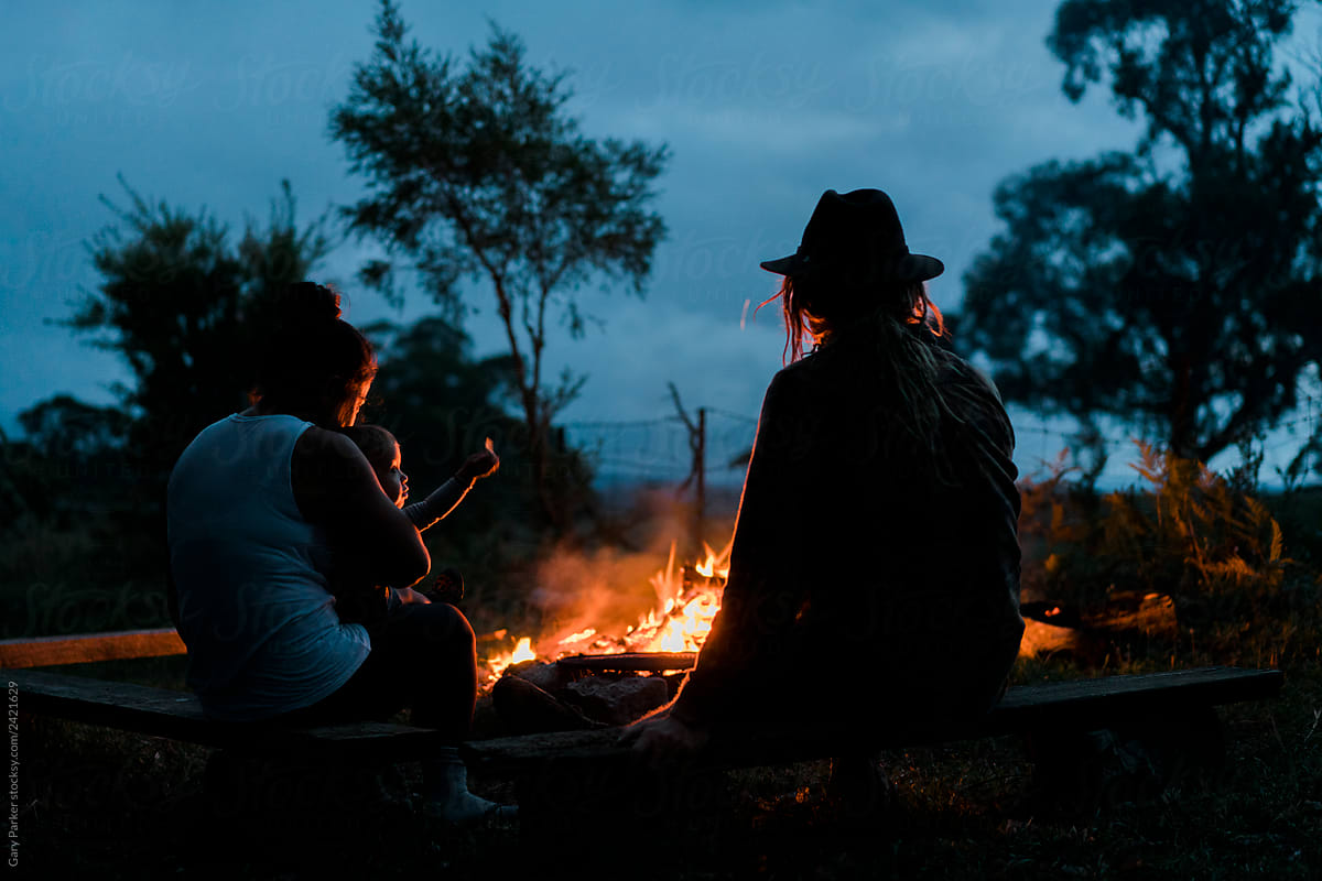 A family sit beside a campfire as the sun goes down
