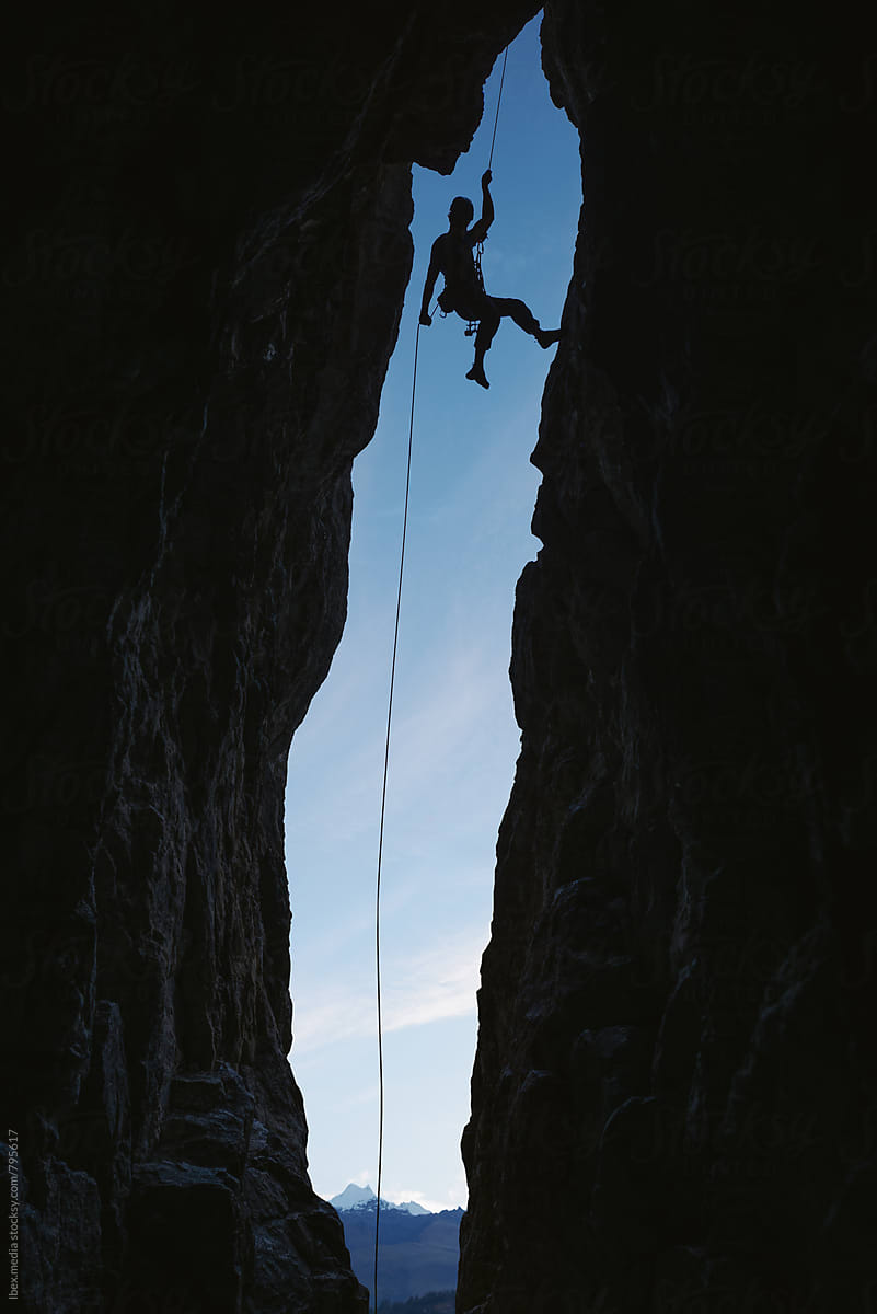 Male alpinist abseiling from the top of a cave